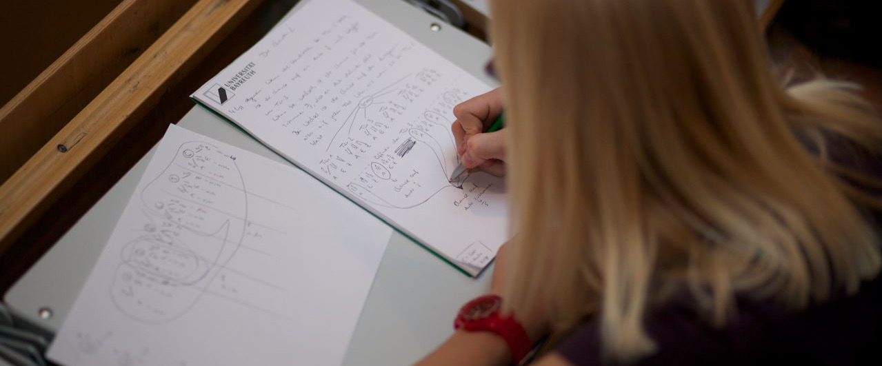 Studentin schreibt beim Tag der Mathematik auf ein Blatt Papier.
